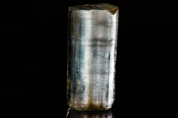 Vertical prismatic blue aquamarine crystal standing with a partial reflection.
