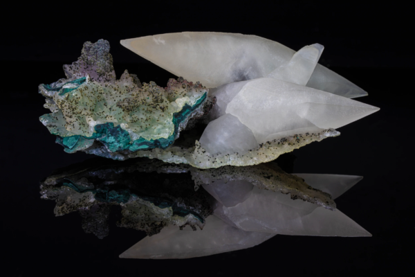 Translucent white calcite crystals on green matrix from Brazil with reflection.