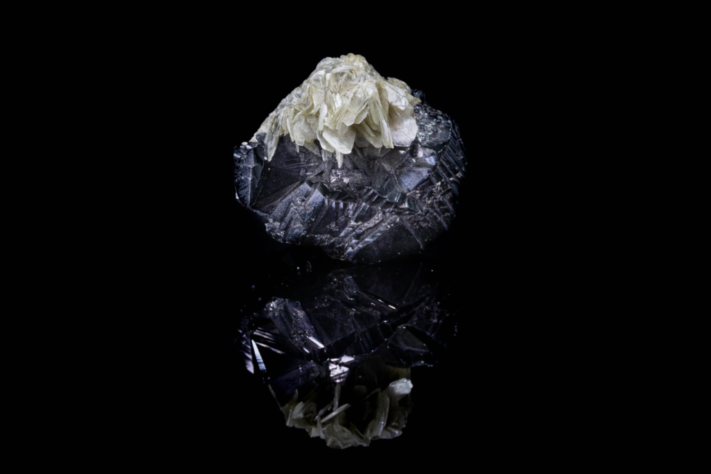 Pale green muscovite on black cassiterite crystal from China with reflection.