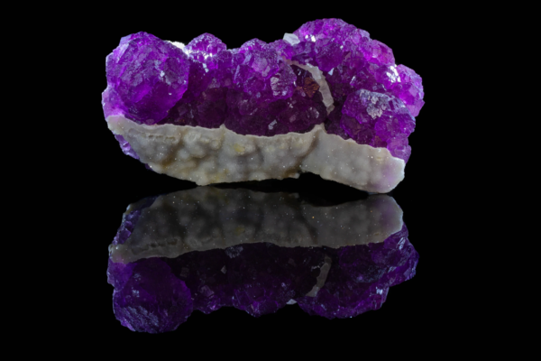 Purple fluorite crystal cluster on white botryoidal matrix with reflection.