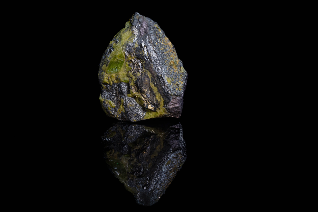 Black metallic ilmenite with green titanite displaying a vertical reflection.