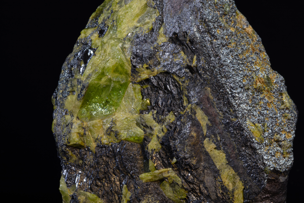 Macro view of a translucent green titanite crystal next to ilmenite.