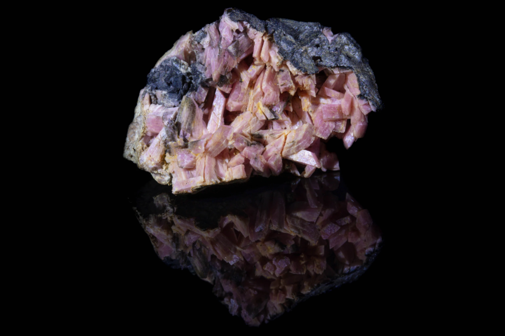 Pink prismatic inesite crystal cluster displaying a sharp mirror reflection.